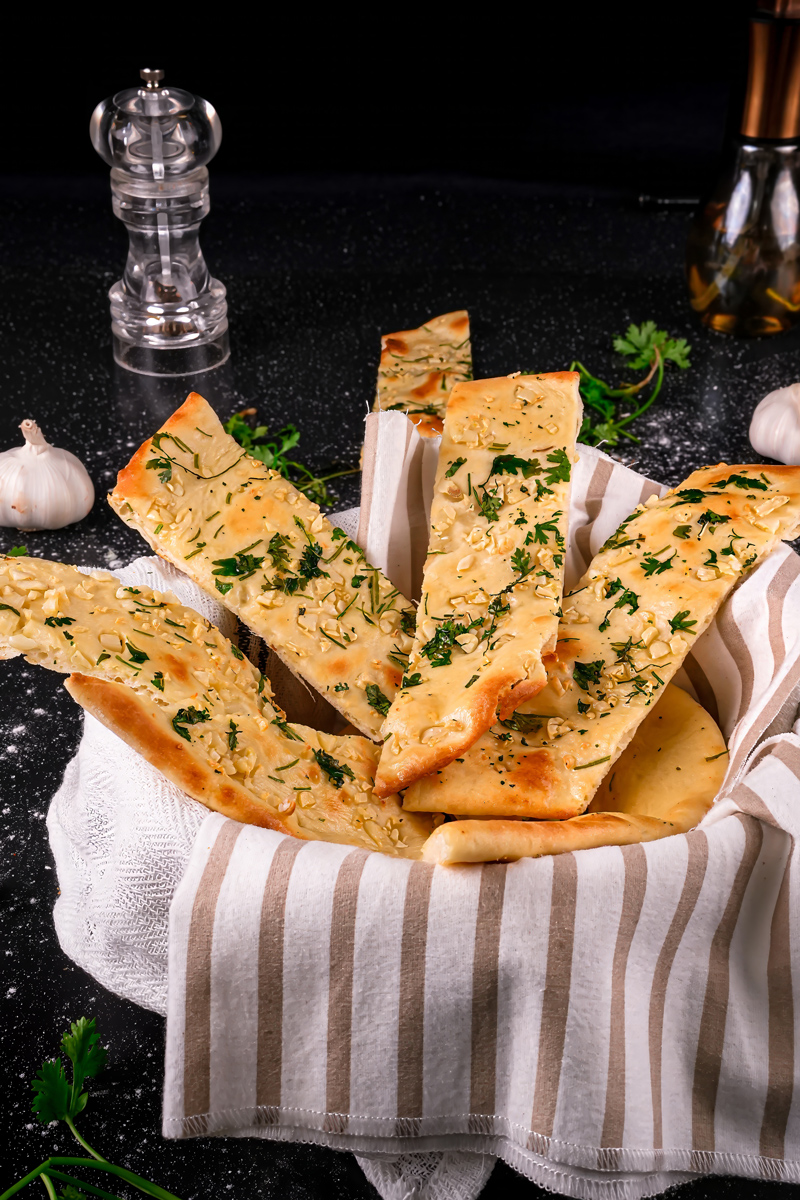 Close-up of crispy garlic naan slices garnished with herbs.