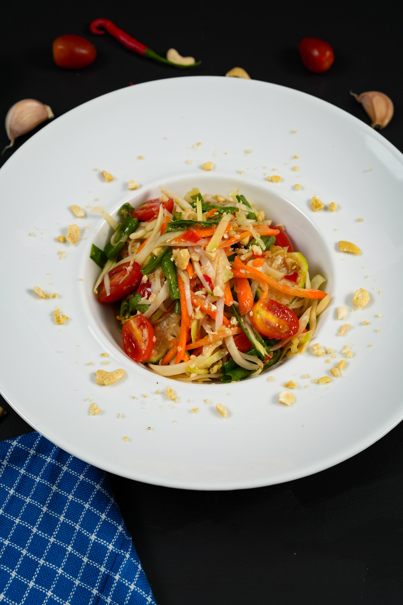 Customization Green Papaya Salad in a white bowl, garnished with crushed peanuts and fresh vegetables.