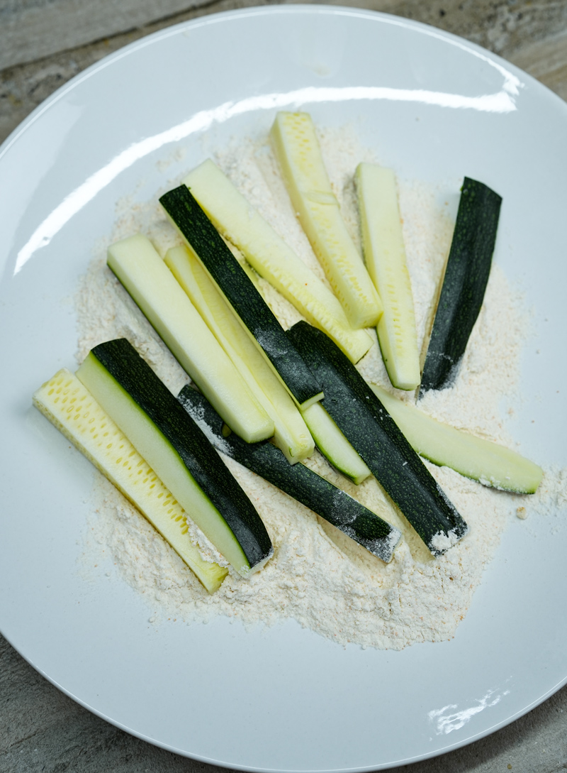 Zucchini sticks lightly coated in flour for frying.