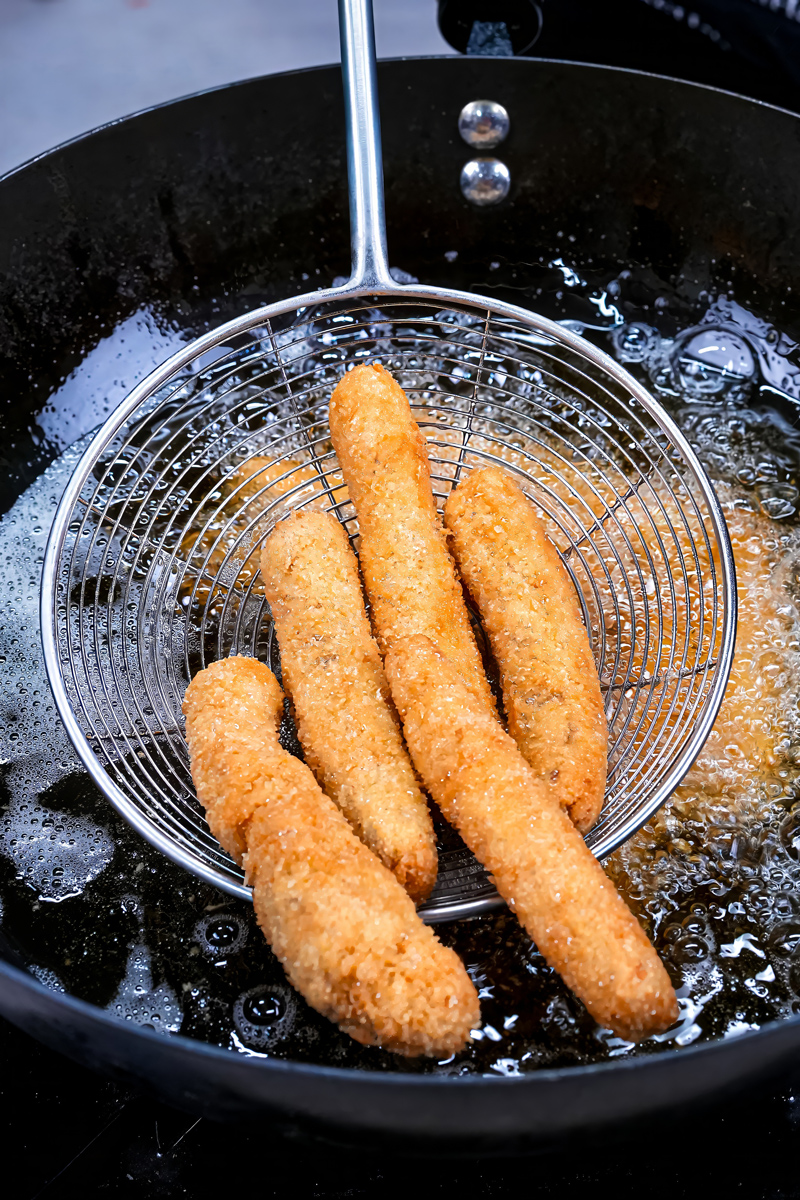 Golden brown fried fish sticks being removed from oil.