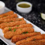 Fish sticks on a plate with lime wedges and green dipping sauce.