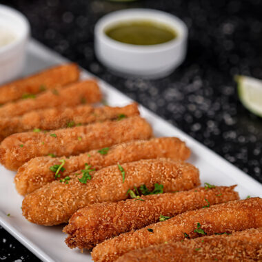 Fish sticks on a plate with lime wedges and green dipping sauce.