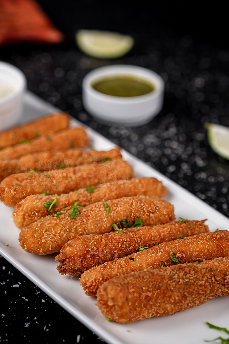 Fish sticks on a plate with lime wedges and green dipping sauce.