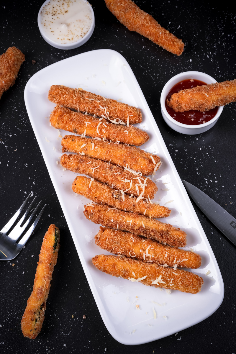 Crispy fried zucchini on a plate with a fork and dipping sauce.