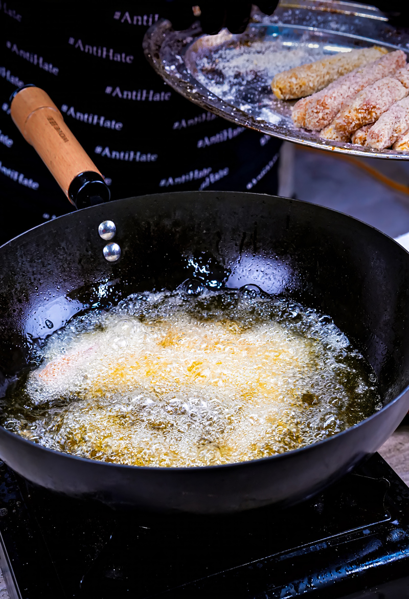 Fish sticks being fried in hot oil in a black pan.