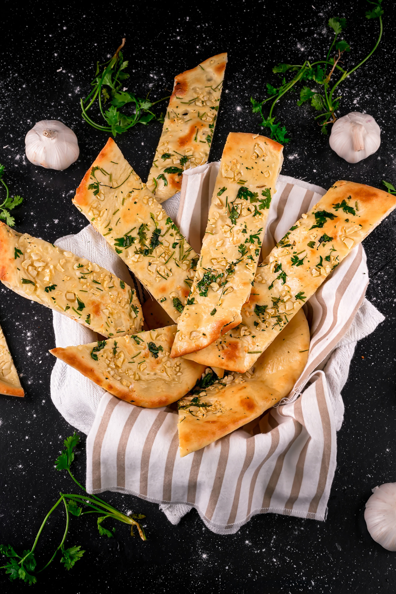 Sliced garlic naan served in a basket with garlic cloves.