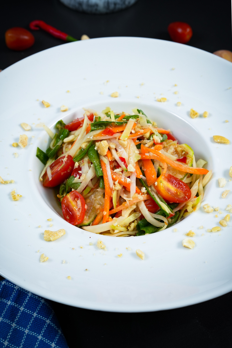 Vibrant Green Papaya Salad served with fresh ingredients and garnished with peanuts in a white plate.