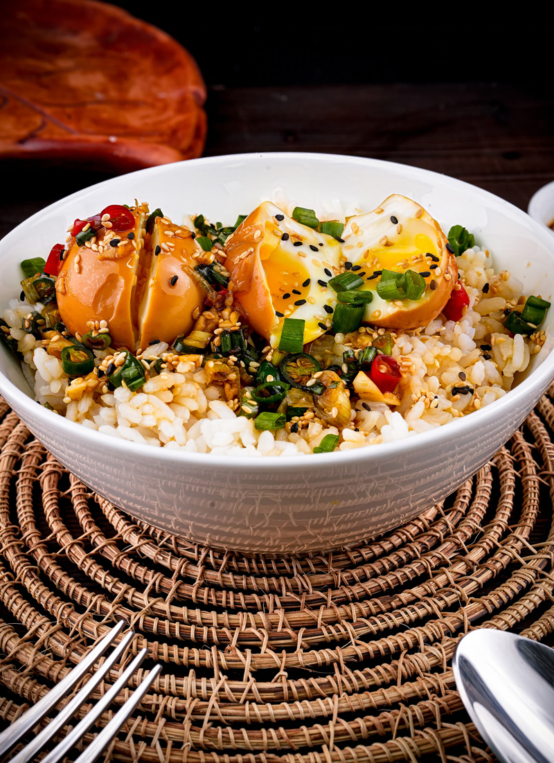 Side view of Mayak Eggs on rice in a white bowl with colorful toppings.