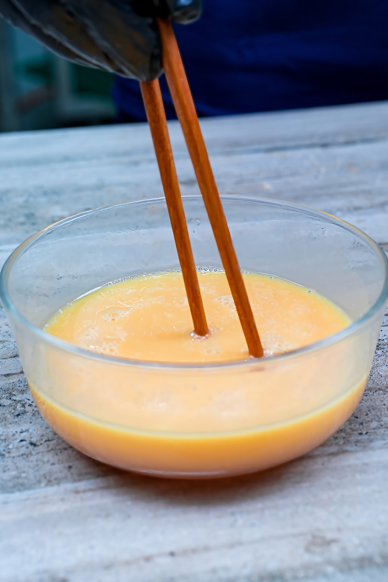 Mixing scrambled eggs in a glass bowl with chopsticks.