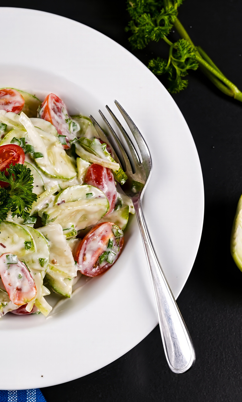 Side view of creamy cucumber tomato salad showcasing fresh herbs and vegetables.