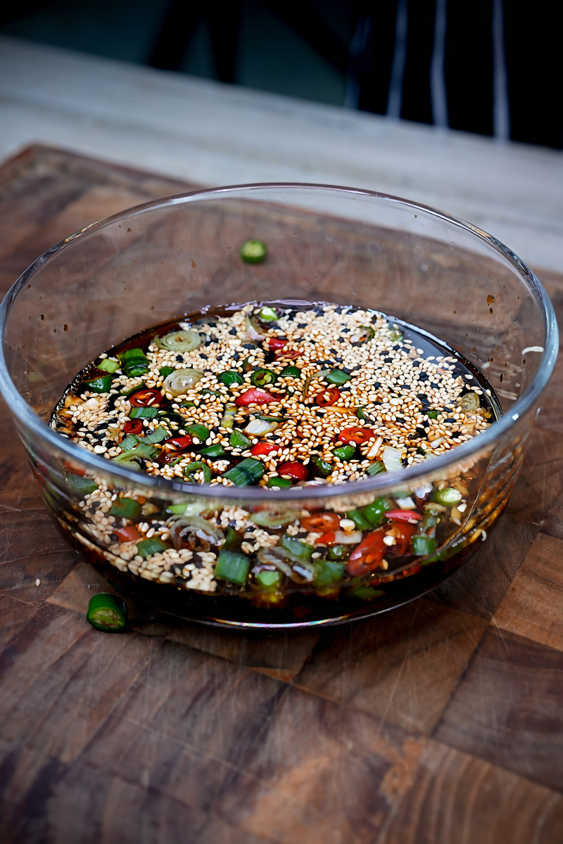 Bowl of soy sauce marinade with sesame seeds, chilies, and scallions for Mayak Eggs.