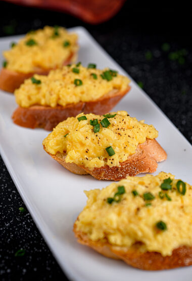 Perfectly arranged scrambled eggs on toast with a dark, elegant backdrop.