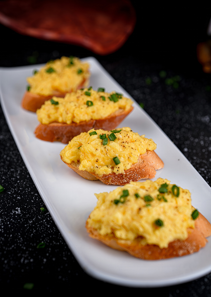 Plated scrambled eggs toast in a neat row, garnished with green onions.