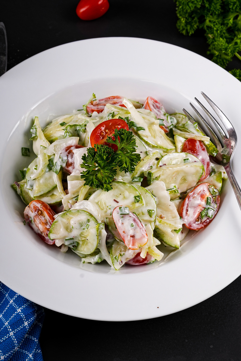 Creamy cucumber tomato salad served in a white bowl with a fork.