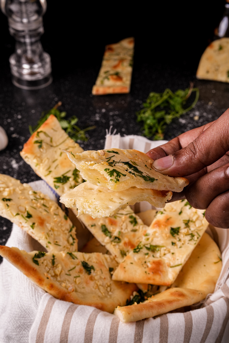 Hand holding a piece of soft and fluffy garlic naan.