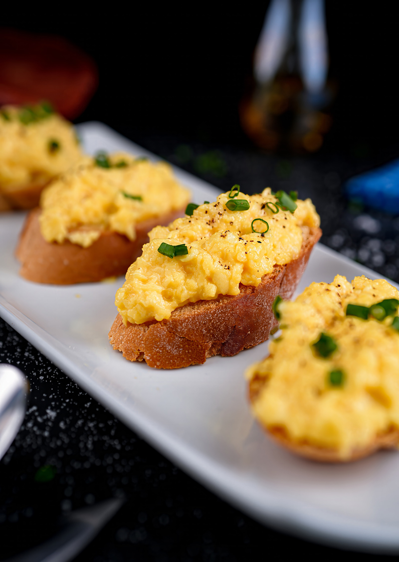 Side view of scrambled eggs toast, served on a white plate with cutlery.