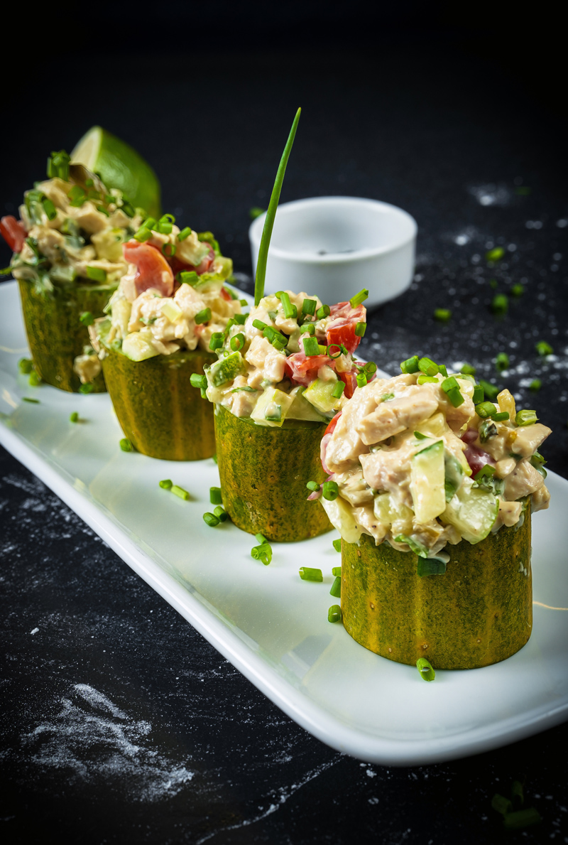 Chicken salad cucumber cups with lime and black pepper in the background.