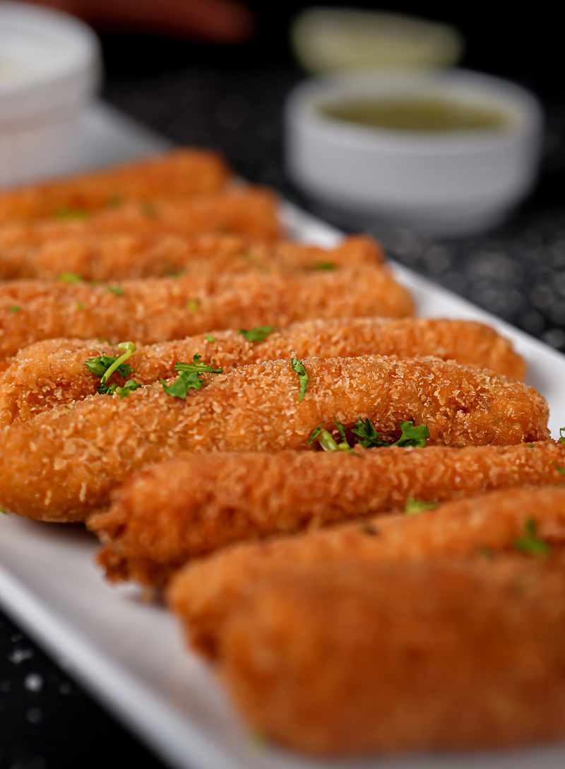 Crispy fish sticks served on a white plate with dipping sauces.