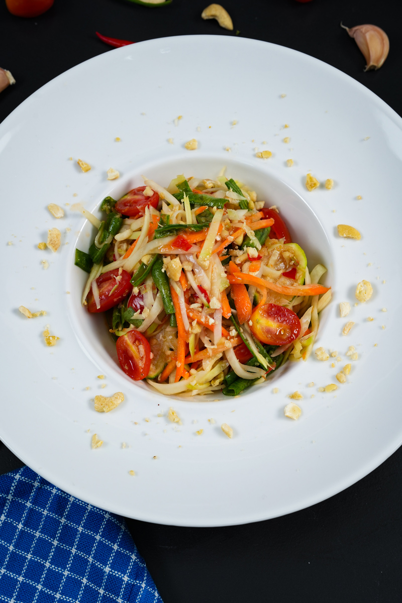 Freshly served Green Papaya Salad in a white bowl with a blue napkin.