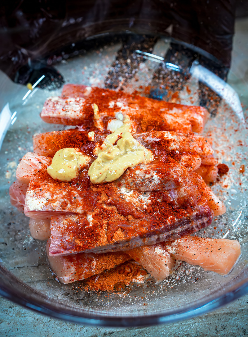 Fish fillets marinated with spices and mustard in a glass bowl.