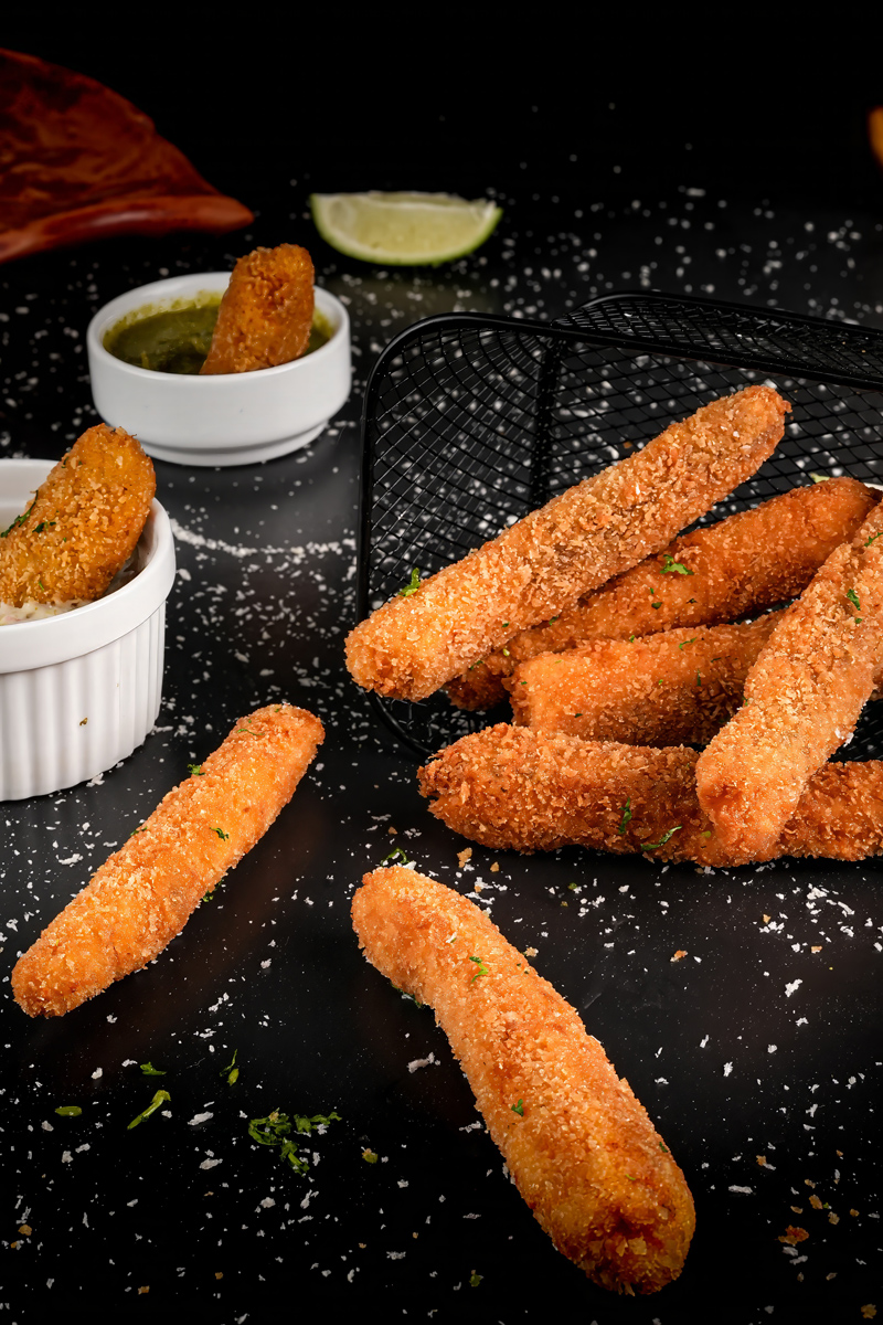 Fish sticks in a serving basket with dipping sauces and lime wedges.