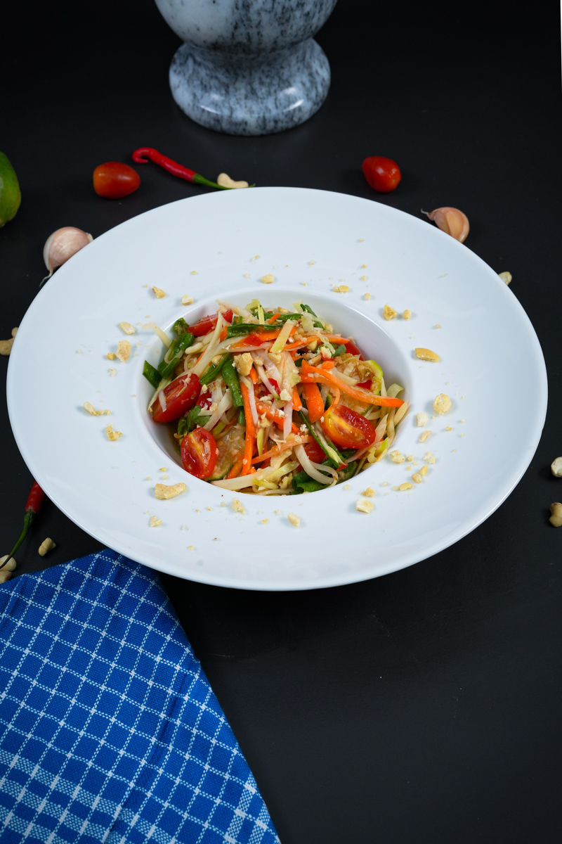 Close-up of Green Papaya Salad in a white bowl with colorful vegetables and crushed peanuts.