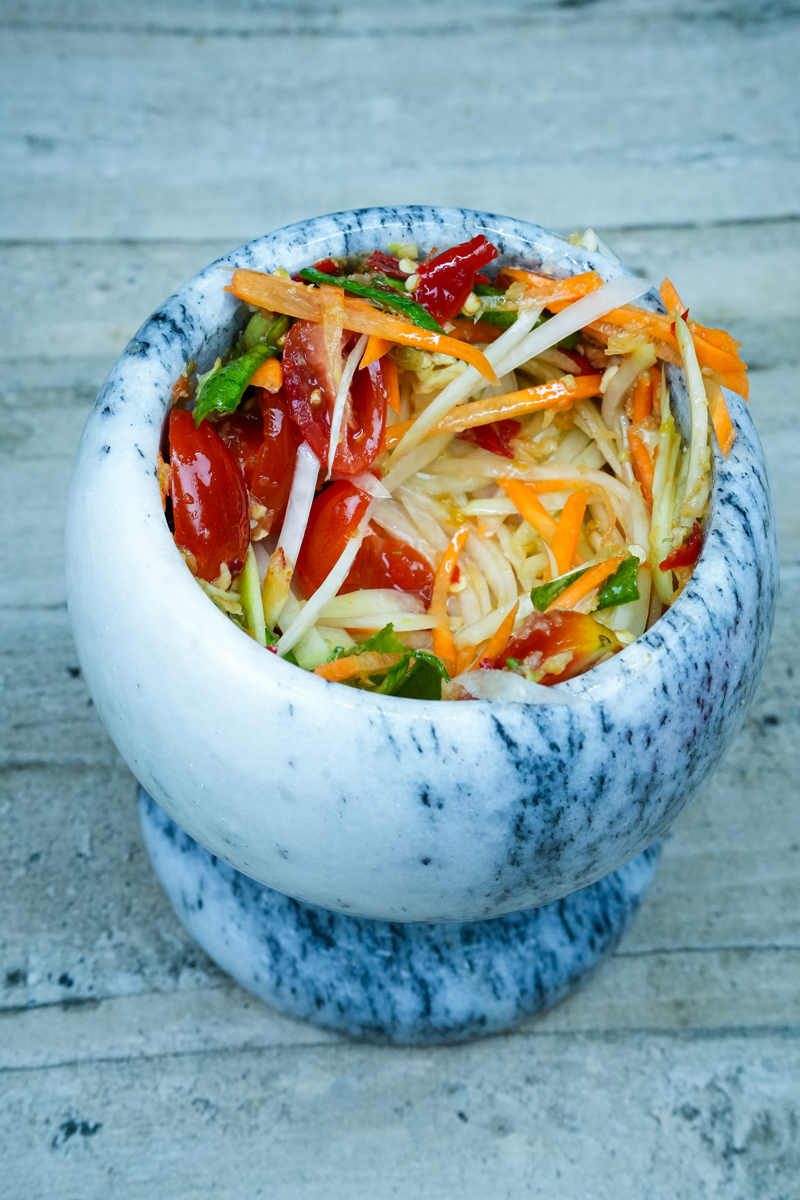 Green Papaya Salad mixed in a marble mortar, featuring vibrant colors of shredded papaya, carrots, and tomatoes.