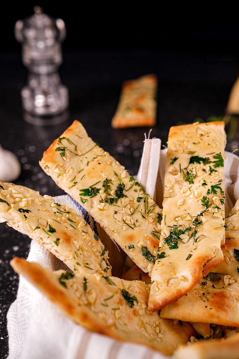 Basket of garlic naan slices with herbs and garlic decoration.