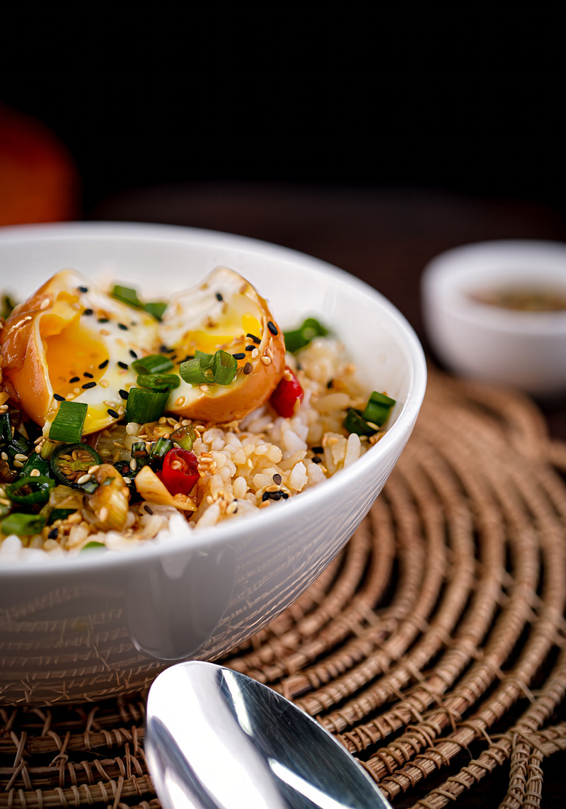 Close-up of Mayak Eggs served over rice with garnishes of green onions and sesame seeds.