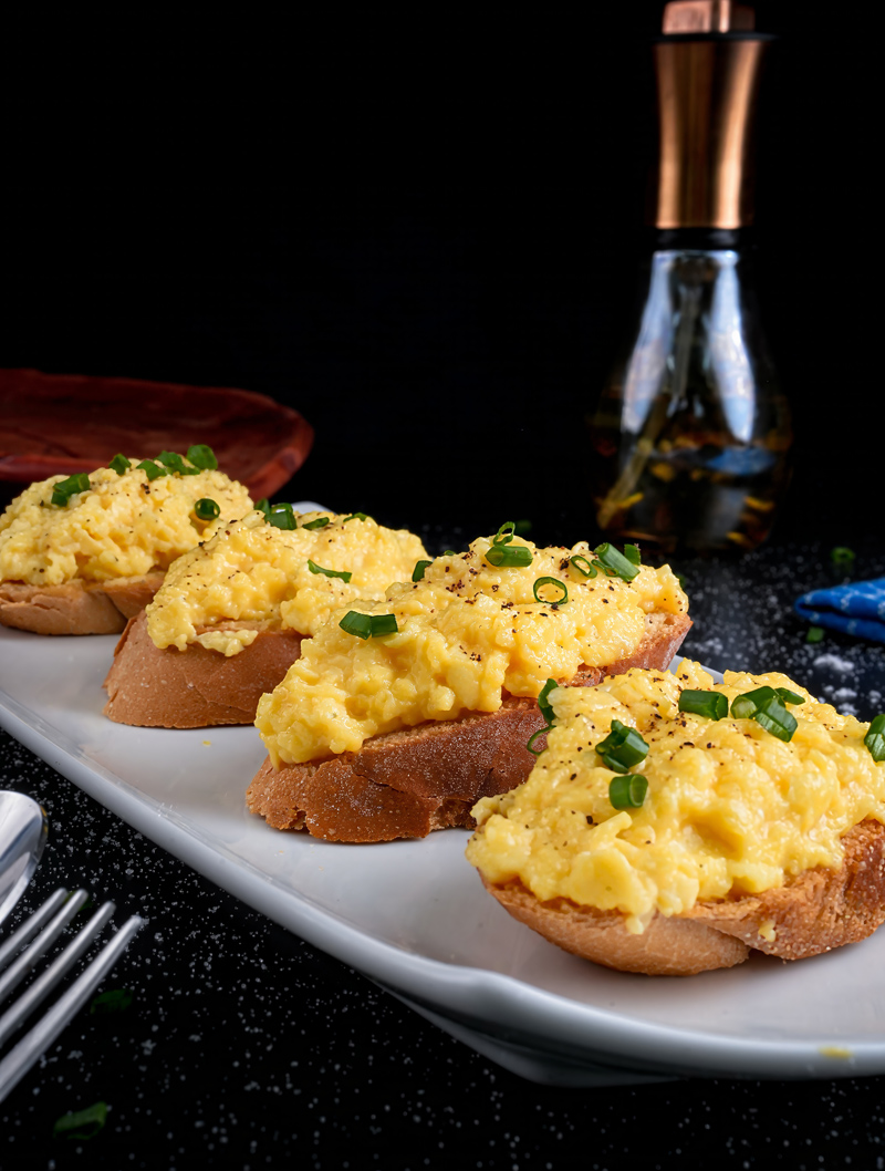 Plated scrambled eggs on toast garnished with green onions on a white dish.