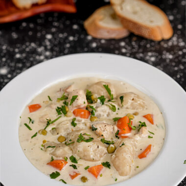 Rich and hearty creamy chicken stew with dumplings, garnished with fresh parsley, served with bread.