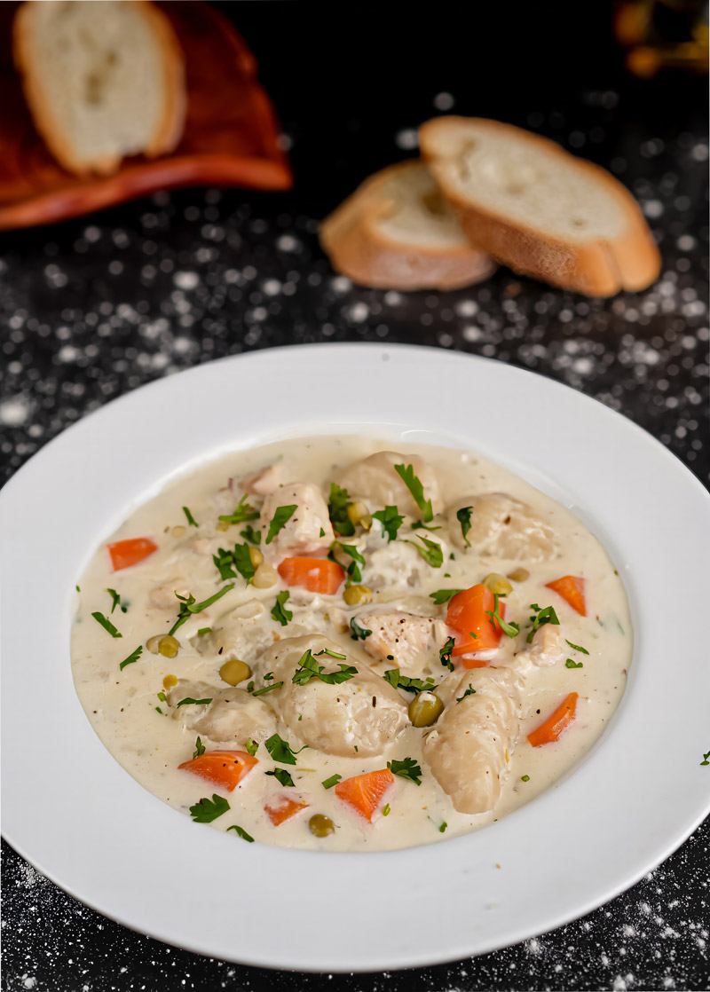 Rich and hearty creamy chicken stew with dumplings, garnished with fresh parsley, served with bread.