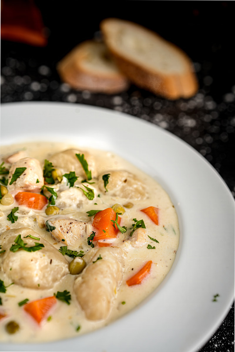 Side angle of homemade chicken and dumplings in a creamy sauce, highlighting tender dumplings and vegetables.