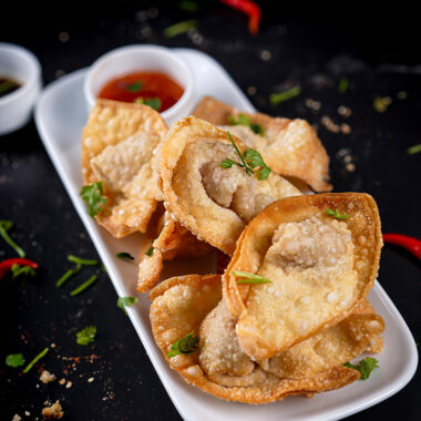 Golden crispy fried shrimp wontons served on a white plate with dipping sauce.