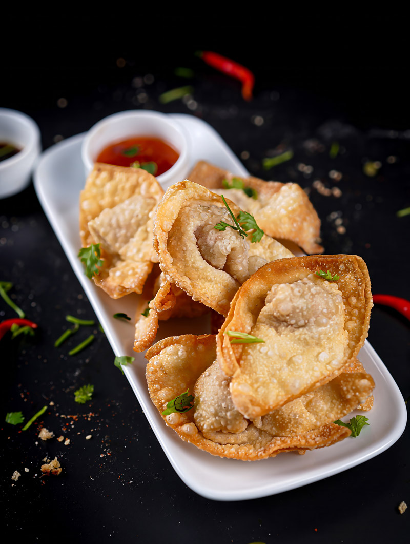 Golden crispy fried shrimp wontons served on a white plate with dipping sauce.