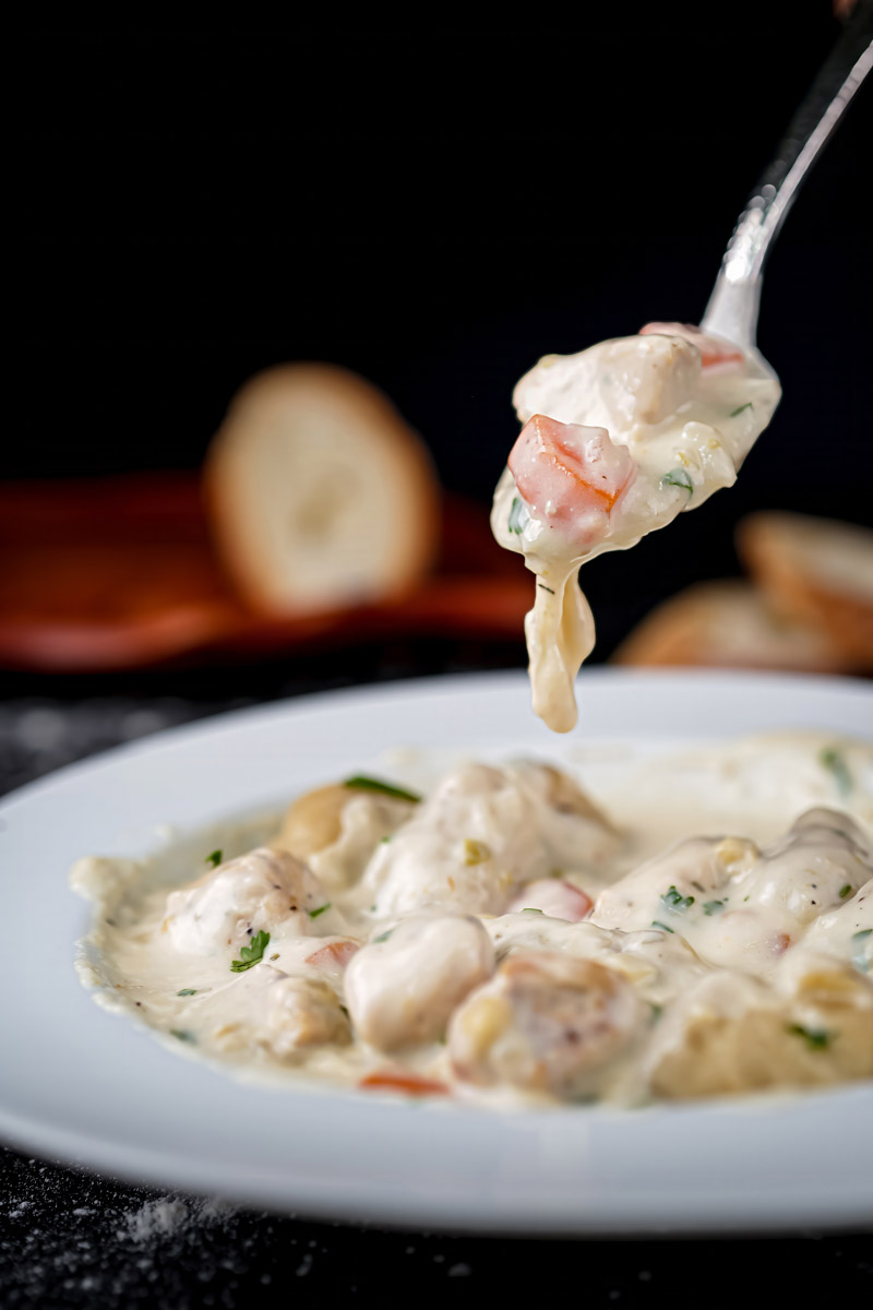 Lifting a bite of creamy chicken and dumplings, revealing chunks of chicken, dumplings, and carrots in sauce.