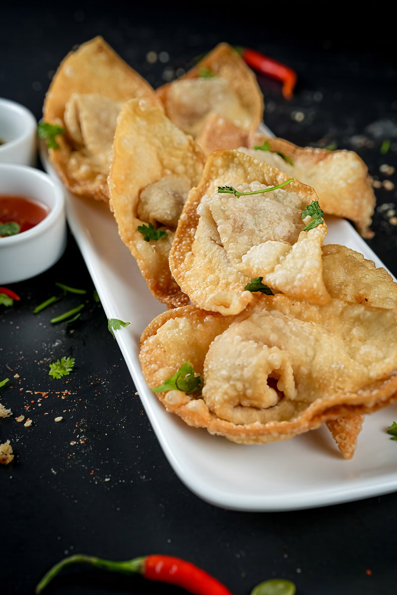 Deep-fried shrimp wontons paired with a chili dip on a dark rustic setup.