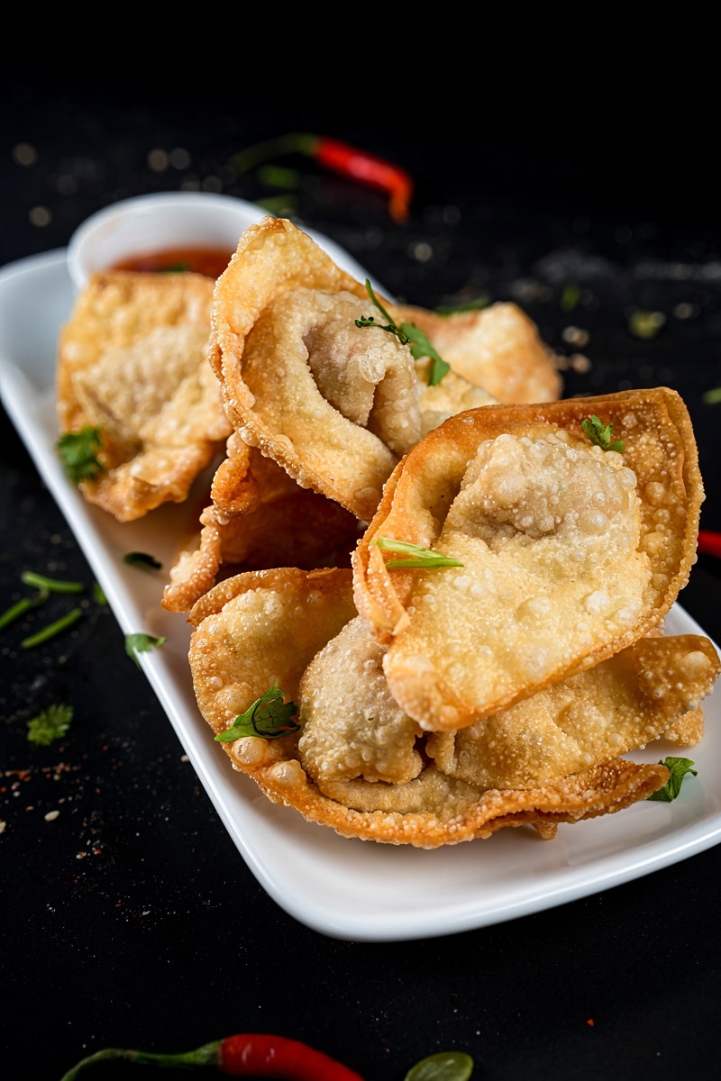 Crunchy shrimp-filled wontons plated with chili sauce on a black background.