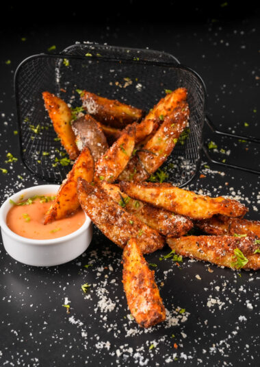 Crispy seasoned air fryer potato wedges with dipping sauce in wire basket