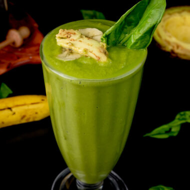 Nutritious green smoothie topped with banana slice and spinach leaf