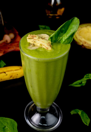 Nutritious green smoothie topped with banana slice and spinach leaf