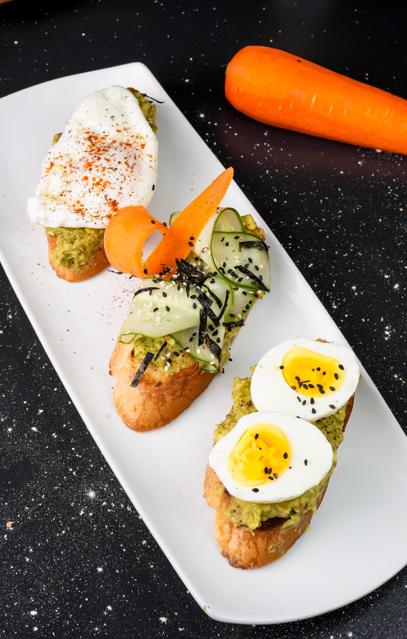 Avocado toast plate with egg and vegetable toppings on dark background