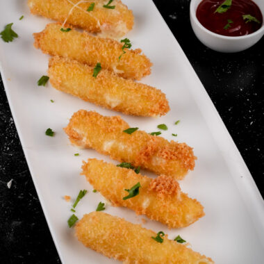 Close-up of mozzarella sticks garnished with parsley on serving plate with dips