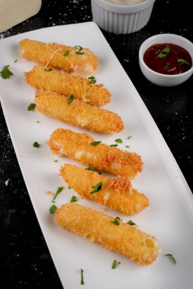 Close-up of mozzarella sticks garnished with parsley on serving plate with dips