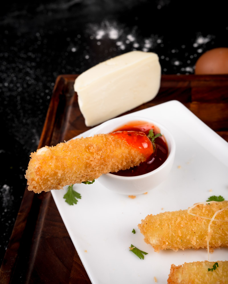 Cheese stick dipped in marinara sauce with block of cheese in background