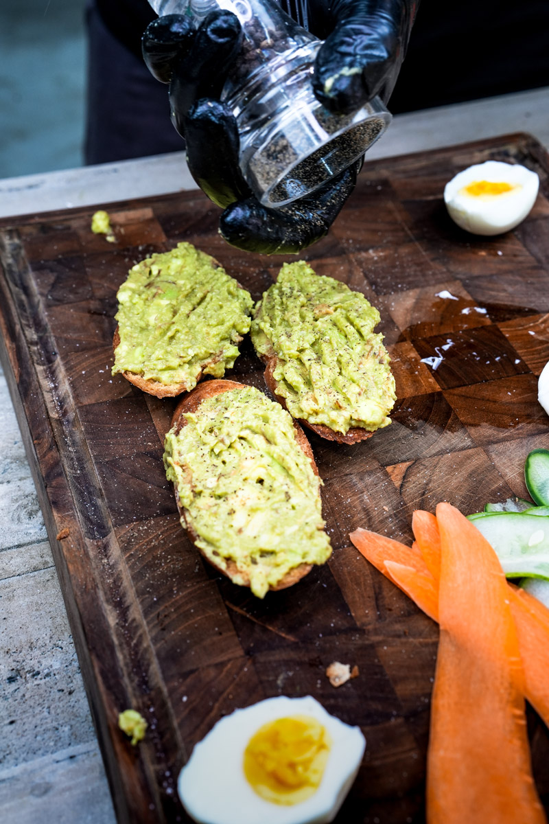 Chef preparing avocado toast with black gloves sprinkling seasoning