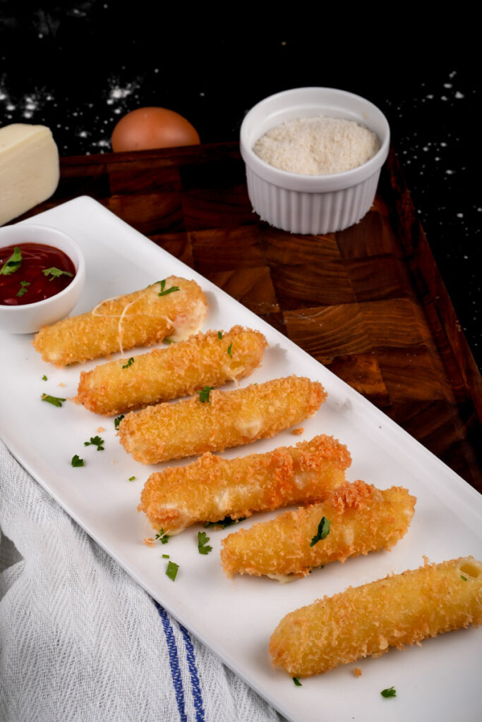 Close-up of mozzarella sticks garnished with parsley on serving plate with dips