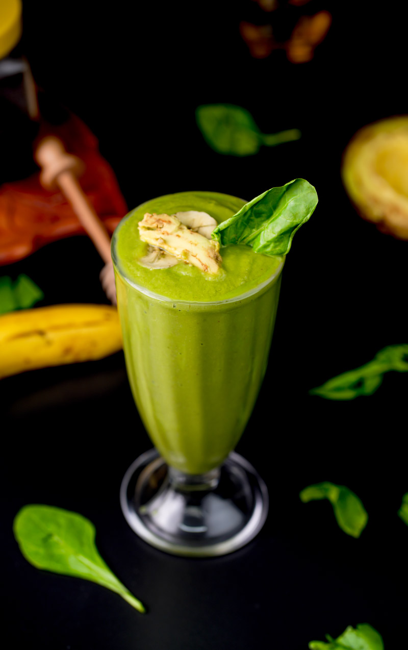 Creamy green avocado spinach smoothie in tall glass with banana garnish