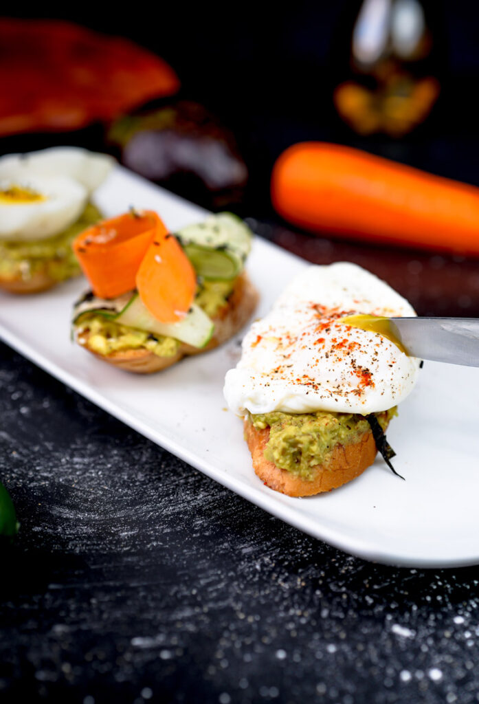 Cutting avocado toast with knife showing runny egg yolk