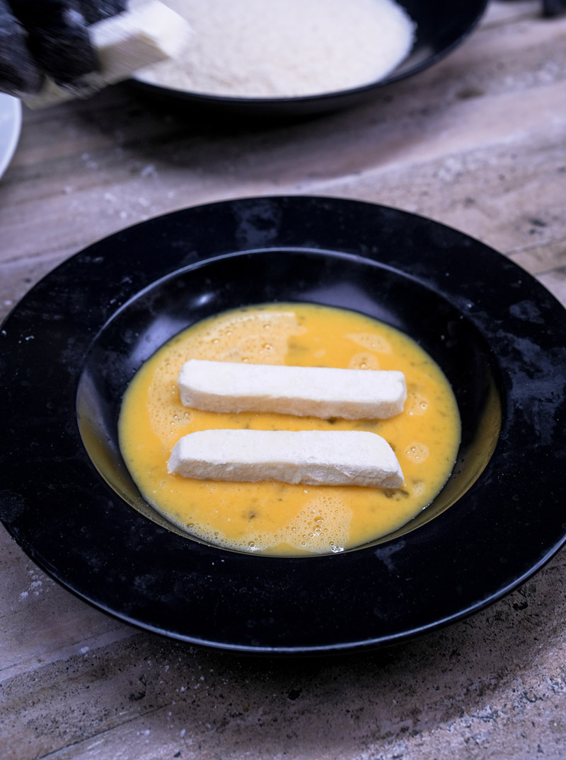Dipping raw cheese sticks in beaten egg mixture before breading
